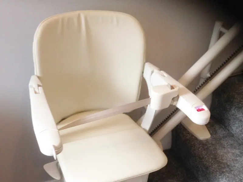 Cream stairlift chair folded against the wall of a home staircase