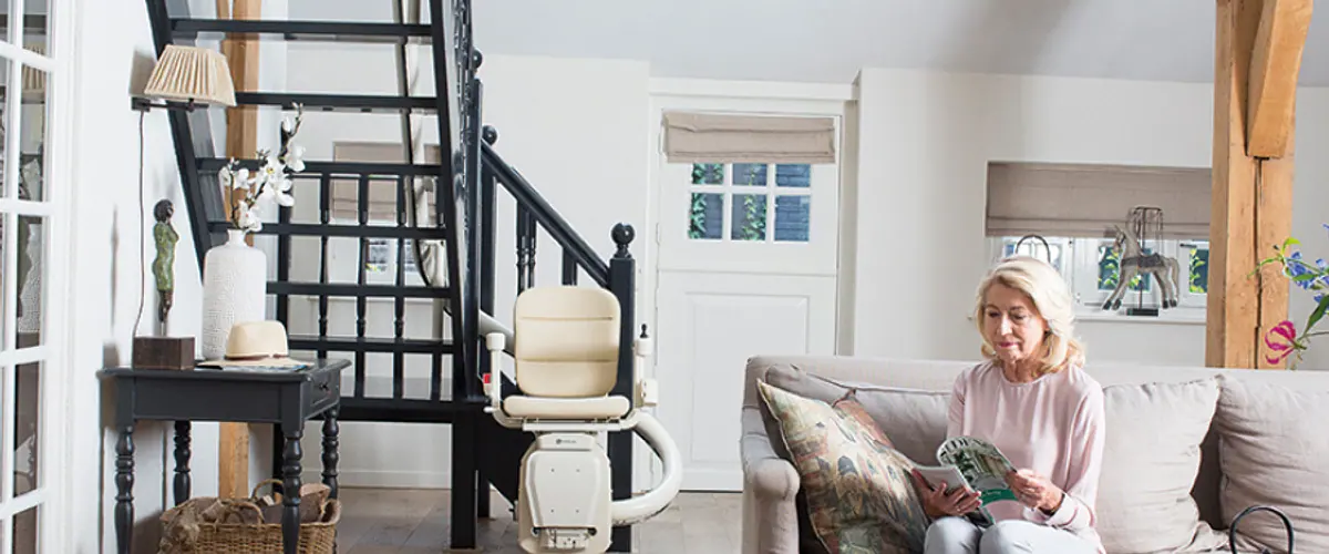 Older woman relaxing at home near her straight stairlift in a bright living room