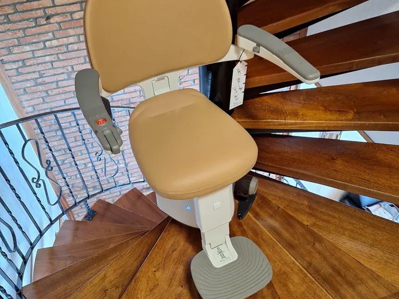 Tan curved stairlift following the bend of a wooden spiral staircase