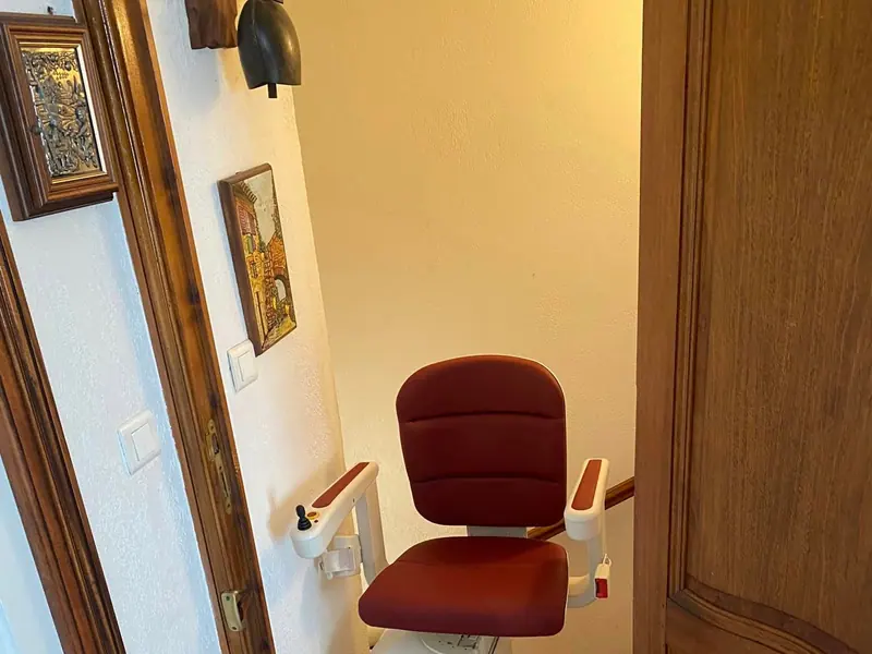 Heavy-duty burgundy stairlift with a wide padded seat on a home staircase