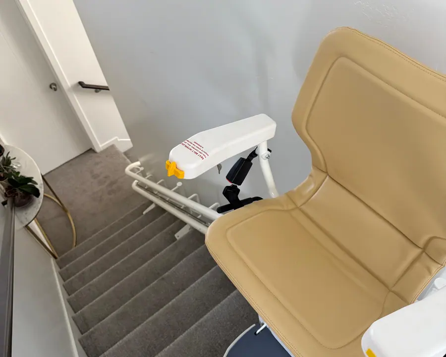 Beige straight stairlift parked at the bottom of a carpeted staircase